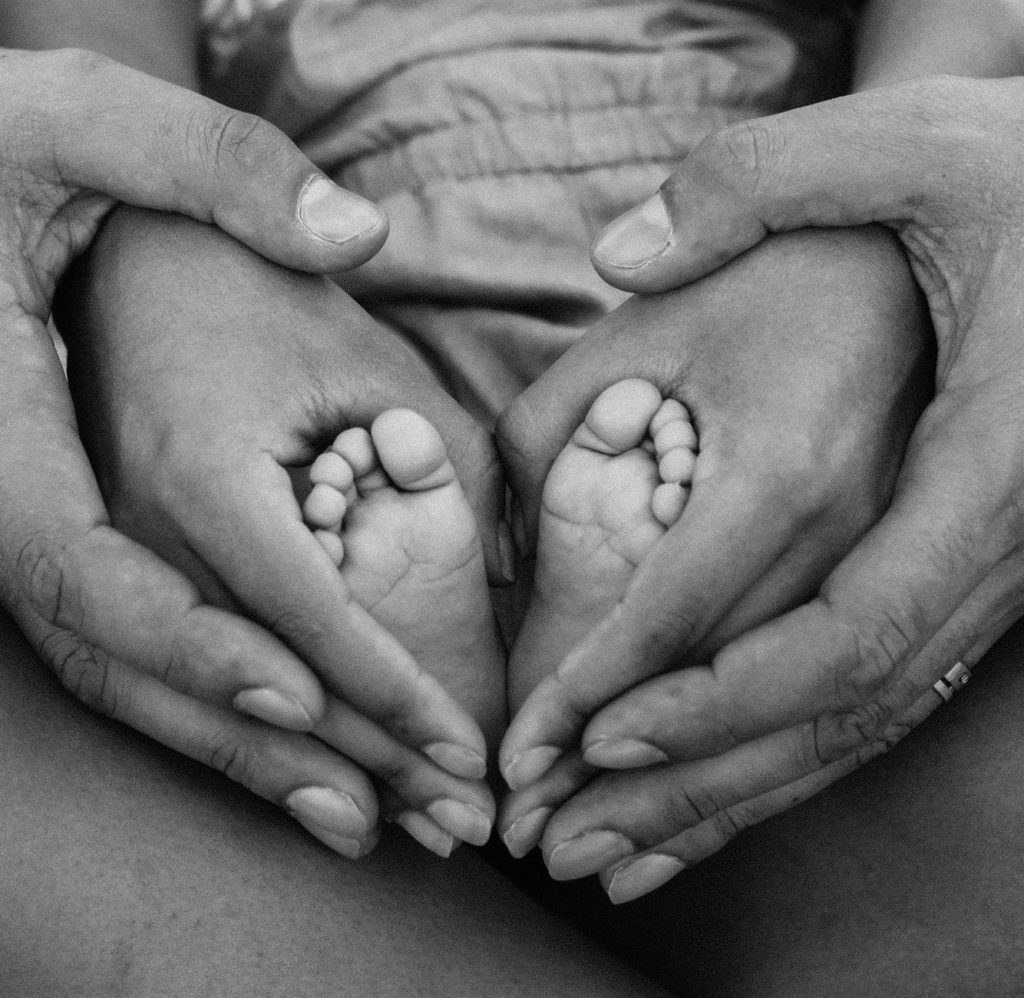 A black and white photo of a man and woman holding a baby's feet.