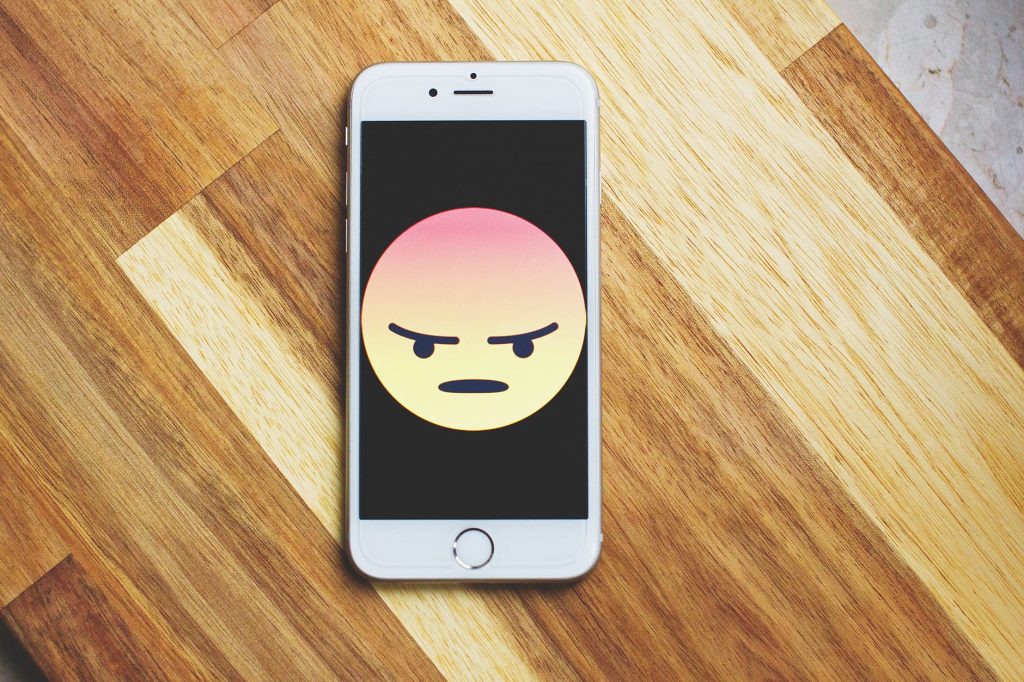 A white iphone with an angry emoji face on the screen.
