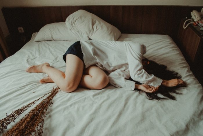 A woman lies on a bed, she is suffering.